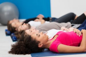 Aerobics class practising deep breathing for relaxation lying on their backs on their mats on the floor with focus to a young African American woman in the foreground